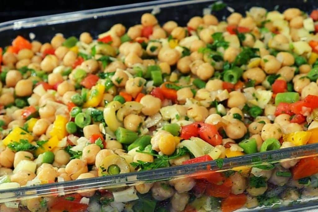 A salada de grão de bico é uma escolha perfeita para quem busca uma refeição leve, saudável e cheia de sabor. Ideal para almoços e jantares, essa salada também acompanha outros pratos com maestria. Além de nutritiva, ela é fácil de fazer e pode ser preparada com antecedência, o que a torna uma opção prática para o dia a dia. O segredo dessa receita está na combinação de ingredientes frescos e coloridos, que juntos criam uma explosão de sabores e texturas irresistíveis.Ingredientes para a Salada de Grão de BicoAntes de começarmos a preparar essa deliciosa salada, vamos conferir todos os ingredientes necessários. Cada um deles desempenha um papel importante, contribuindo para o sabor, a textura e o valor nutricional do prato.500g de grão-de-bico: Rico em proteínas e fibras, o grão-de-bico é a base da nossa salada. Ele oferece uma textura agradável e um sabor suave que combina perfeitamente com os outros ingredientes.1 pimentão amarelo picado: O pimentão amarelo adiciona um toque de doçura e uma cor vibrante à salada. Além disso, ele é rico em vitamina C e antioxidantes.100g de vagem picada cozida: A vagem traz uma crocância leve e um sabor fresco, além de ser uma excelente fonte de vitaminas e minerais.1 cenoura em cubos cozida: A cenoura adiciona uma doçura natural e uma cor laranja vibrante à salada. Ela também é rica em betacaroteno, que é bom para a visão e a pele.50g de ervilha fresca congelada: A ervilha contribui com sua cor verde brilhante e um sabor adocicado. Além disso, é uma boa fonte de proteínas vegetais.2 tomates sem sementes picados: Os tomates trazem um toque de acidez e suculência, além de serem ricos em licopeno, um antioxidante poderoso.1 cebola média picada: A cebola adiciona um sabor picante e uma textura crocante, equilibrando os sabores da salada.100g de azeitonas verdes picadas: As azeitonas verdes dão um toque salgado e um sabor marcante que contrasta bem com os outros ingredientes.50ml de vinagre: O vinagre é essencial para temperar a salada, trazendo acidez e ajudando a realçar os sabores dos ingredientes.Azeite, orégano, pimenta-do-reino, sal e salsinha a gosto: Esses temperos são responsáveis por dar o toque final à salada. O azeite adiciona riqueza e suavidade, o orégano traz um aroma herbáceo, a pimenta-do-reino dá um leve toque de calor, e a salsinha adiciona frescor e cor.Queijo coalho picado (opcional): Se você deseja adicionar uma dose extra de sabor e textura, o queijo coalho é uma excelente escolha. Ele traz um sabor levemente salgado e uma textura que combina muito bem com o grão-de-bico.Modo de Preparo da Salada de Grão de BicoAgora que temos todos os ingredientes prontos, é hora de preparar essa deliciosa salada. O processo é simples e rápido, e o resultado é um prato que pode ser servido como prato principal ou como acompanhamento.1. Preparação do Grão de BicoO primeiro passo para preparar essa salada é hidratar e cozinhar o grão-de-bico. Para isso, coloque o grão-de-bico em uma bacia grande e cubra com água. Adicione um pouco de vinagre à água e deixe de molho de um dia para o outro. Esse processo de hidratação é importante para amolecer o grão-de-bico e reduzir o tempo de cozimento.No dia seguinte, escorra a água do molho e transfira o grão-de-bico para uma panela de pressão. Cubra com água fresca até que o grão-de-bico esteja completamente submerso. Leve a panela ao fogo médio-alto, sem tampar, e deixe a água ferver. Assim que a água começar a ferver, descarte a água e adicione nova água na panela, cobrindo o grão-de-bico com aproximadamente dois dedos de água.Tampe a panela de pressão e cozinhe por cerca de 5 minutos após começar a chiar. Esse tempo é suficiente para cozinhar o grão-de-bico, deixando-o macio, mas ainda firme o suficiente para manter sua forma na salada.Após o tempo de cozimento, desligue o fogo e deixe a pressão sair naturalmente. Abra a panela e verifique o ponto do grão-de-bico. Se estiver no ponto certo, escorra e reserve.2. Preparação dos Outros IngredientesEnquanto o grão-de-bico está cozinhando, você pode preparar os outros ingredientes da salada. Comece cozinhando a vagem e a cenoura em água salgada até que estejam macias, mas ainda crocantes. Isso deve levar cerca de 5 a 7 minutos. Escorra e deixe esfriar.Descongele a ervilha fresca congelada, deixando-a em temperatura ambiente por alguns minutos ou mergulhando-a em água morna por alguns instantes. Reserve.Pique o pimentão amarelo, os tomates (lembrando de retirar as sementes) e a cebola em pedaços pequenos. Pique também as azeitonas verdes e o queijo coalho, se for usar.3. Montagem da SaladaAgora que todos os ingredientes estão prontos, é hora de montar a salada. Em uma travessa grande, coloque o grão-de-bico cozido e acrescente a vagem, a cenoura, a ervilha, o pimentão, os tomates, a cebola e as azeitonas.Tempere a salada com azeite, vinagre, orégano, pimenta-do-reino e sal a gosto. Se desejar, adicione o queijo coalho picado. Misture bem todos os ingredientes para que os temperos sejam distribuídos uniformemente.4. Resfriamento e FinalizaçãoApós temperar a salada, leve-a à geladeira por pelo menos 2 horas antes de servir. Esse tempo de descanso permite que os sabores se misturem e a salada fique ainda mais saborosa e refrescante.Na hora de servir, você pode finalizar com um pouco mais de azeite e salsinha fresca picada por cima. A salada de grão de bico está pronta para ser saboreada!Dicas e Variações para Personalizar a Salada de Grão de BicoA salada de grão de bico é extremamente versátil e pode ser adaptada de acordo com o seu gosto pessoal ou os ingredientes que você tem em casa. Aqui estão algumas sugestões para você experimentar:Adicione Proteína: Se quiser tornar a salada ainda mais nutritiva, experimente adicionar uma fonte de proteína como peito de frango desfiado, atum em conserva ou até mesmo cubos de tofu grelhado.Varie os Vegetais: Substitua ou adicione outros vegetais conforme sua preferência. Abobrinha, pepino, rabanete e espinafre fresco são ótimas opções para diversificar a salada.Use Diferentes Temperos: Além do orégano e da pimenta-do-reino, você pode experimentar outros temperos como cominho, páprica defumada, curry em pó ou até um pouco de alho picado para dar mais sabor à salada.Experimente Outras Ervas Frescas: Além da salsinha, outras ervas frescas como coentro, manjericão ou hortelã podem adicionar um toque de frescor à salada.Sirva com Molho: Se você quiser um toque extra de sabor, sirva a salada com um molho à parte. Um molho à base de iogurte com limão e alho, ou um vinagrete balsâmico, são ótimas opções.Como Armazenar a Salada de Grão de BicoA salada de grão de bico é excelente para ser preparada com antecedência, pois seus sabores ficam ainda melhores após algumas horas de descanso. Se você preparar a salada e não consumi-la toda, ela pode ser armazenada na geladeira por até 3 dias.Para armazenar, coloque a salada em um recipiente hermético e mantenha na geladeira. Se a salada estiver temperada com vinagre e azeite, ela manterá sua textura e sabor por mais tempo. Evite congelar, pois os vegetais podem perder sua textura crocante após o descongelamento.Conclusão: Uma Salada de Grão de Bico Que SatisfazA salada de grão de bico é uma escolha excelente para qualquer refeição, seja como prato principal ou como acompanhamento. Rica em nutrientes, cheia de sabores e texturas, e incrivelmente fácil de preparar, essa salada é perfeita para os dias quentes de verão ou para qualquer ocasião em que você deseja uma refeição leve e refrescante.Além disso, a versatilidade dessa salada permite que você personalize a receita de acordo com seu gosto, tornando-a uma opção prática e deliciosa para o dia a dia. Então, que tal experimentar essa receita e trazer um toque de frescor para a sua mesa? Tenho certeza de que será um sucesso garantido!